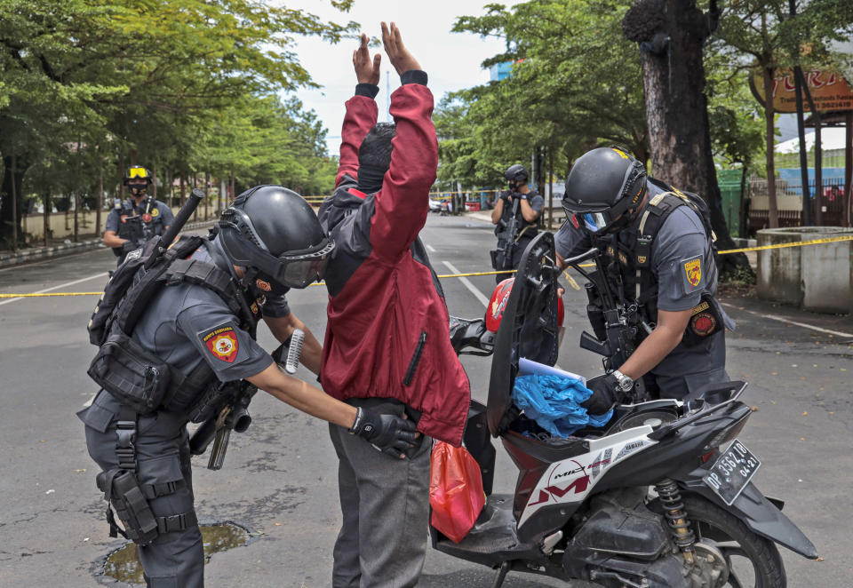 Police officers search a man at a security checkpoint near the site of Sunday's suicide bomb attack at the Sacred Heart of Jesus Cathedral in Makassar, South Sulawesi, Indonesia, Monday, March 29, 2021. Two attackers believed to be members of a militant network that pledged allegiance to the Islamic State group blew themselves up outside the packed Roman Catholic cathedral during a Palm Sunday Mass on Indonesia's Sulawesi island, wounding a number of people, police said. (AP Photo/Yusuf Wahil)
