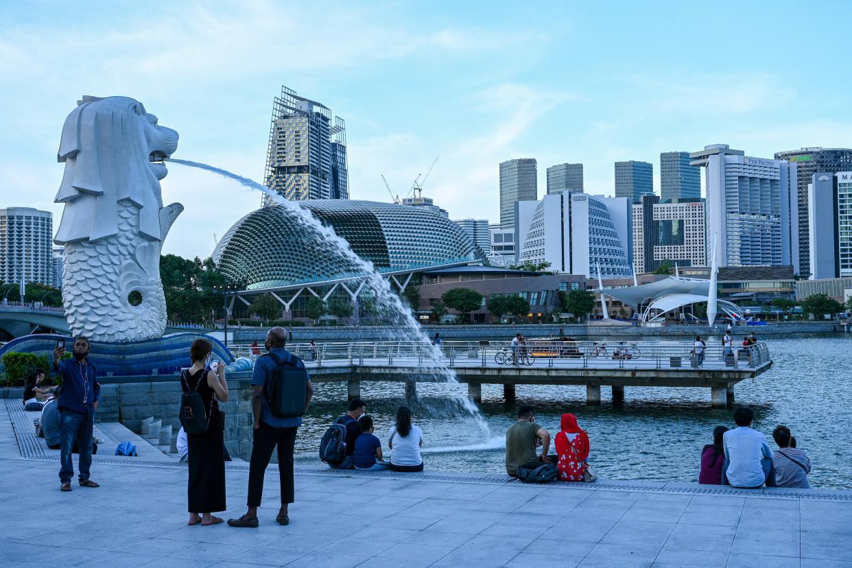 In this photograph taken on February 18, 2022, people relax along the waterfront next to the Merlion statue in Singapore. - Rivals Singapore and Hong Kong have become pandemic polar opposites, the former opting to live with the coronavirus and reopen to the world while the latter doubles down on zero-Covid and its international isolation. - To go with AFP story Health-virus-Hong Kong-China-Singapore, FOCUS by Holmes Chan with Catherine Lai in Singapore (Photo by Roslan RAHMAN / AFP) / To go with AFP story Health-virus-Hong Kong-China-Singapore, FOCUS by Holmes Chan with Catherine Lai in Singapore (Photo by ROSLAN RAHMAN/AFP via Getty Images)