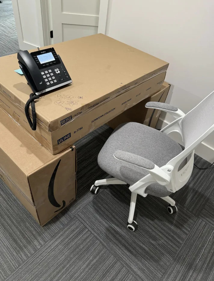 A makeshift desk made of stacked cardboard boxes with a phone on top and an office chair beside it