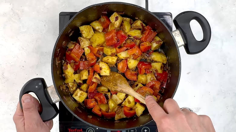 stirring potato and red bell pepper in pan