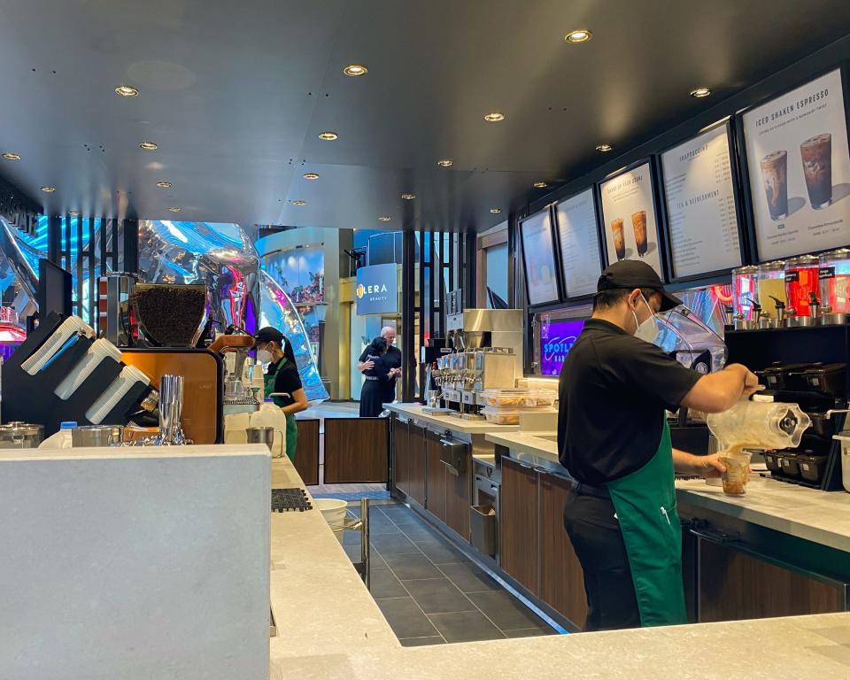 An employee makes a drink behind a counter at a starbucks stand on an indoor deck on a cruise ship