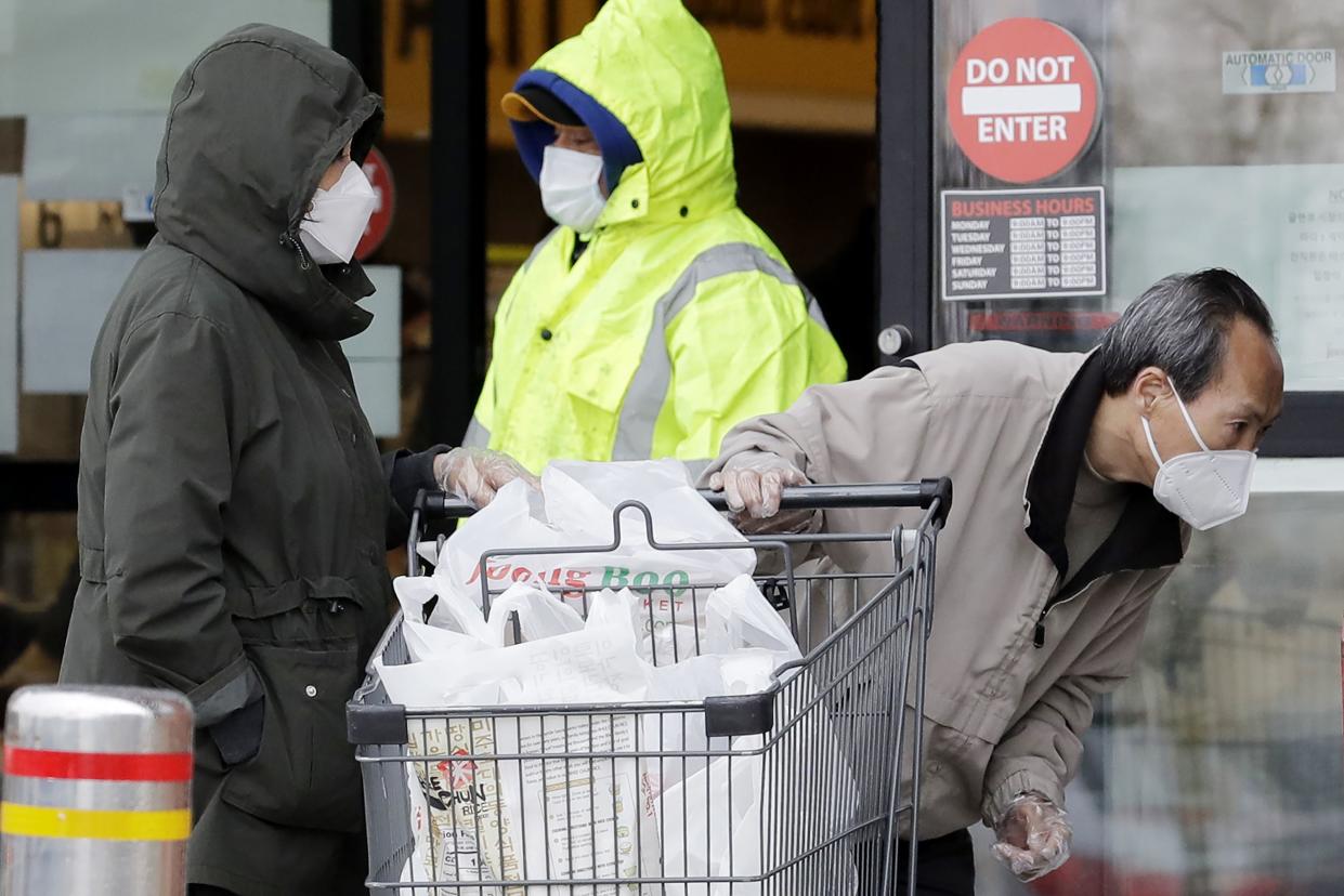 A shopper, right, checks a newspaper vending machine outside a grocery store in Glenview, Ill. on Saturday, April 25, 2020. Illinois Gov. J.B. Pritzker extended a stay-at-home order through May 30 that requires face masks to be worn in public due to the COVID-19 pandemic.