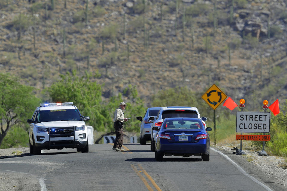 A Pima County Sheriff officer checks residents' identification in a closed off neighborhood affected by the Bighorn Fire along the western side of the Santa Catalina Mountains, Friday, June 12, 2020, in Tucson, Arizona. Hundreds of homes on the outskirts of Tucson remain under an evacuation notice as firefighters work to keep the wildfire from moving downhill from canyons and ridges in the Coronado National Forest. (AP Photo/Matt York)