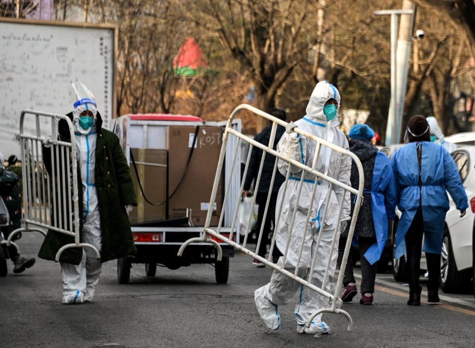 Health workers wearing personal protective equipment (PPE) carry barricades away from a residential community that has just opened after an easing of strict COVID-19 coronavirus restrictions in Beijing, China, December 9, 2022. / Credit: NOEL CELIS/AFP/Getty
