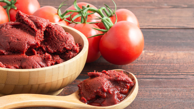 tomato paste in a wood bowl next to fresh tomatoes on a wood surface