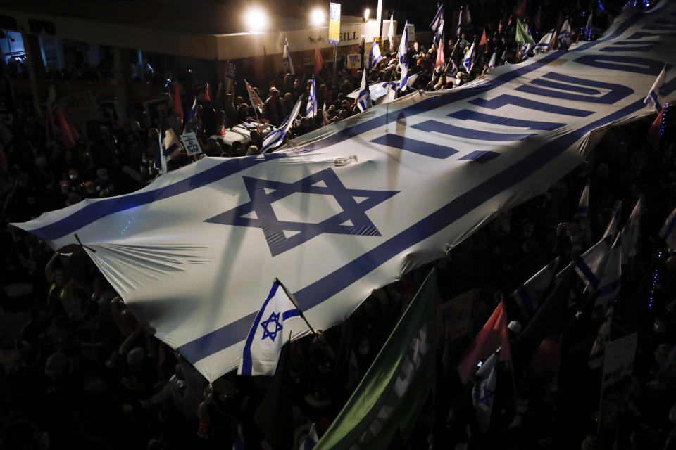 Israeli protesters carry large Israeli flag during a protest against Israel's Prime Minister Benjamin Netanyahu outside his residence in Jerusalem, Saturday, March. 20, 2021. The weekly protests against Netanyahu's corruption charges and his handling of the pandemic have persisted since summer, but tonight's gathering is the last before Israel will be holding its fourth election in two years on March 23. Hebrew on flag reads "it's in our hands". (AP Photo/Sebastian Scheiner)