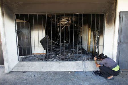 A woman takes pictures of burned debris of the Ombudsman office in Maracaibo, Venezuela May 25, 2017. REUTERS/Isaac Urrutia