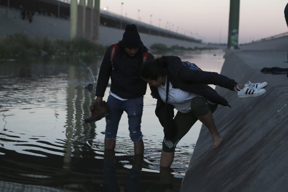 A man in the river helps a woman balance as she enters.