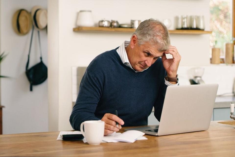 A man concentrates while staring at his laptop while sitting at a wooden desk. 