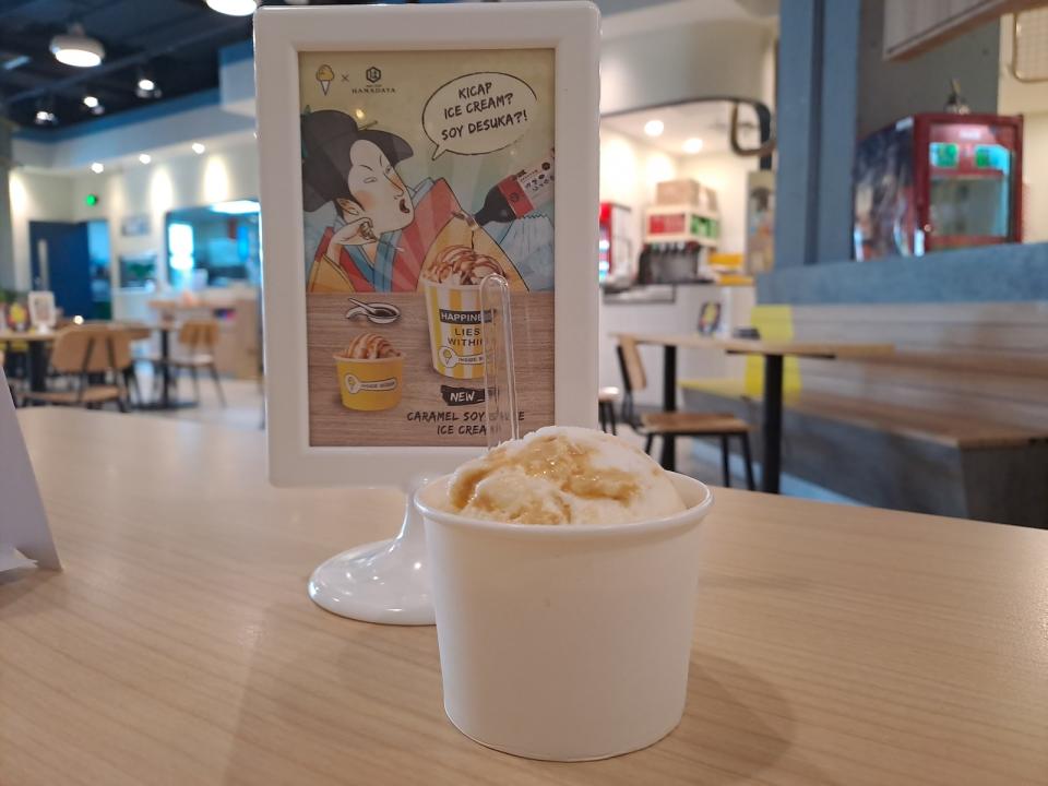 The soy sauce ice cream in a cup on a table beside its promotional pamphlet.