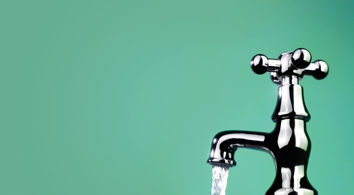  Water coming out of a silver faucet on a teal background. 