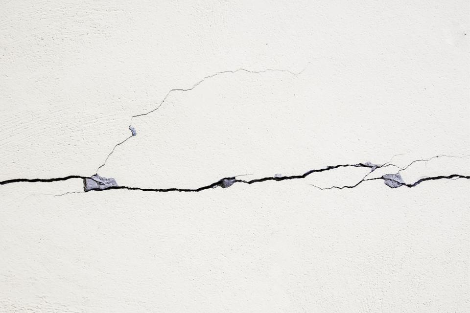 Cracks in a white wall are seen close up.