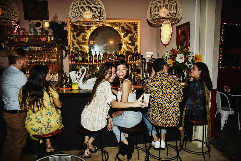 Female friends taking selfie with smart phone while sitting at bar in night club