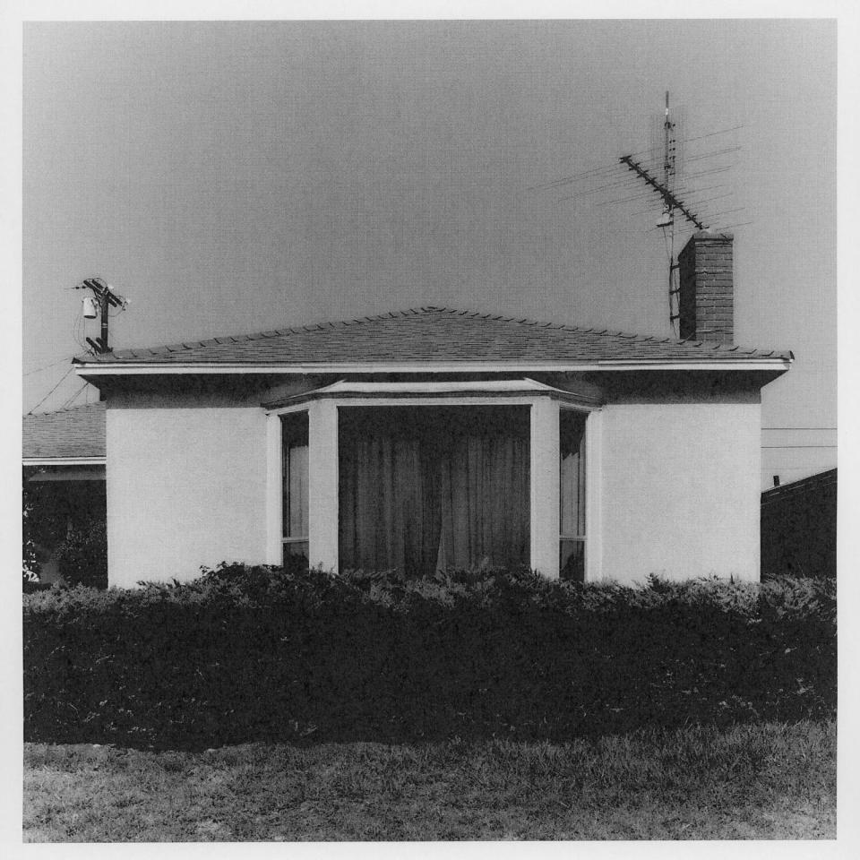 A black and white photo of a house with some bushes in front.
