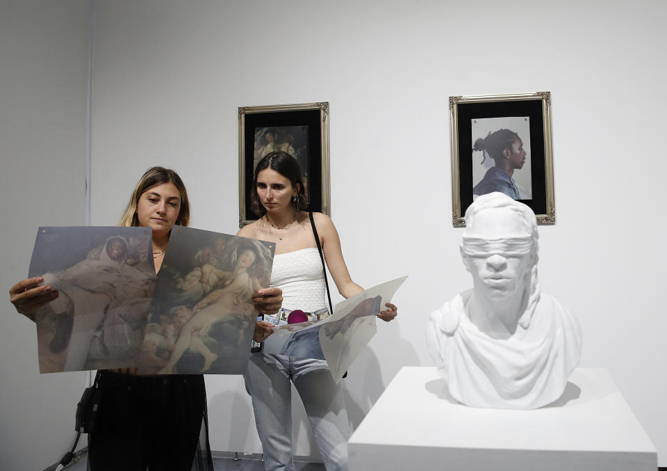 FILE- In this Dec. 6, 2018, file photo, two people look at the artist Hajar Benjida's project called "Young Thug as Paintings" at the Scope Miami Beach gallery during Art Basel in Miami Beach, Fla. According to a statement released Wednesday, Sept. 2, 2020, the Art Basel fair, known for glamorous parties and celebrity sightings, is cancelling its annual Miami event amid the coronavirus pandemic. (AP Photo/Brynn Anderson, File)