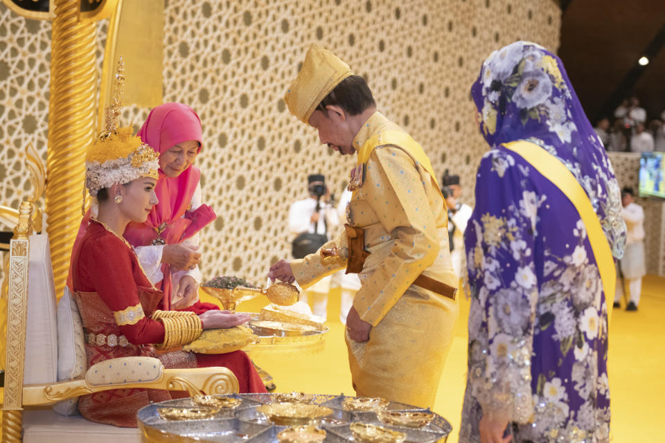 This picture taken by Brunei's Information Department on Jan. 10, 2024 shows Brunei's Sultan Hassanal Bolkiah, centre right, pouring scented oil on the hands of Brunei's Prince Abdul Mateen's bride Yang Mulia Anisha Rosnah, left, during the royal powdering ceremony at Istana Nurul Iman, ahead of his wedding to Anisha Rosnah, in Bandar Seri Begawan, Brunei. (Brunei's Information Department via AP)