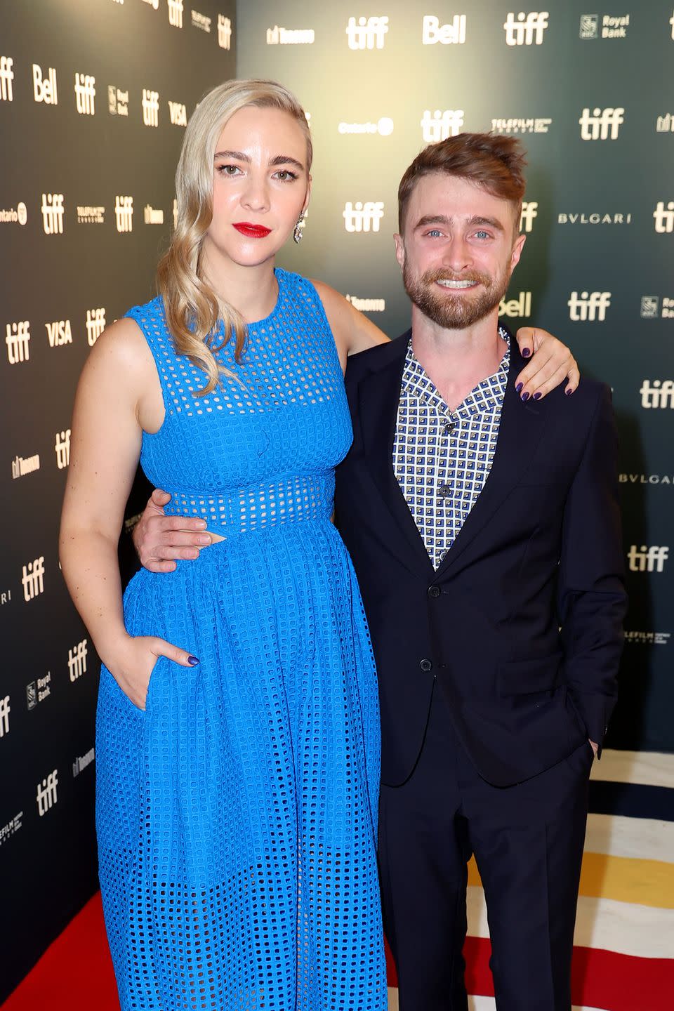 erin darke in a blue dress with daniel radcliffe who is wearing a black suit and checkered tie