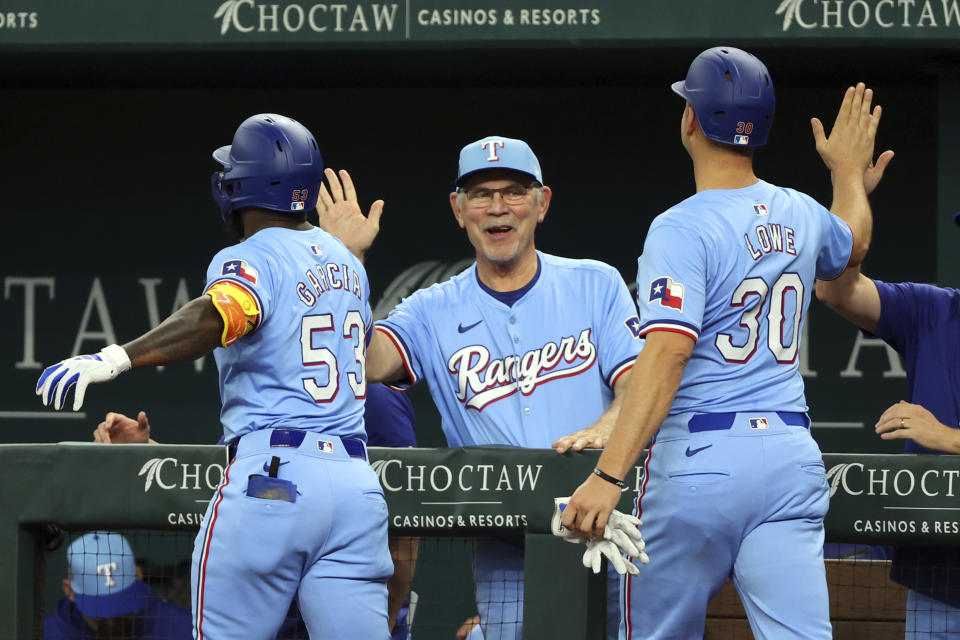 Texas Rangers' Adolis Garcia and Nathaniel Lowe (30) celebrate with manager Bruce Bochy, center, after Garcia's two-run home run against the Cincinnati Reds in the first inning of a baseball game Sunday, April 28, 2024, in Arlington, Texas. (AP Photo/Richard W. Rodriguez)