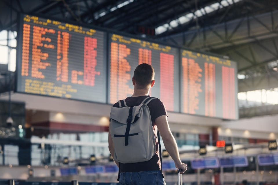 Man walking with backpack and suitcase walking through airport terminal and looking at departure information