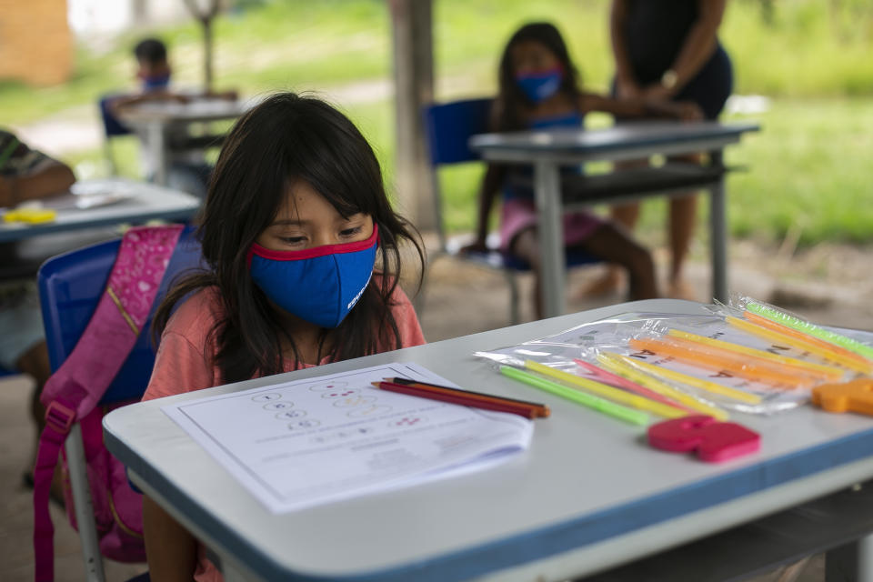 A Guarani girl, wearing a protective face mask, sits at her desk in an open air classroom in the Mata Verde Bonita village, in Marica, Rio de Janeiro state, Brazil, Thursday, Feb. 25, 2021, where healthcare workers are making the rounds with coolers containing doses of China's Sinovac COVID-19 vaccine as part of a mass immunization program aimed at inoculating all of Rio’s 16 million residents by the end of the year. (AP Photo/Bruna Prado)