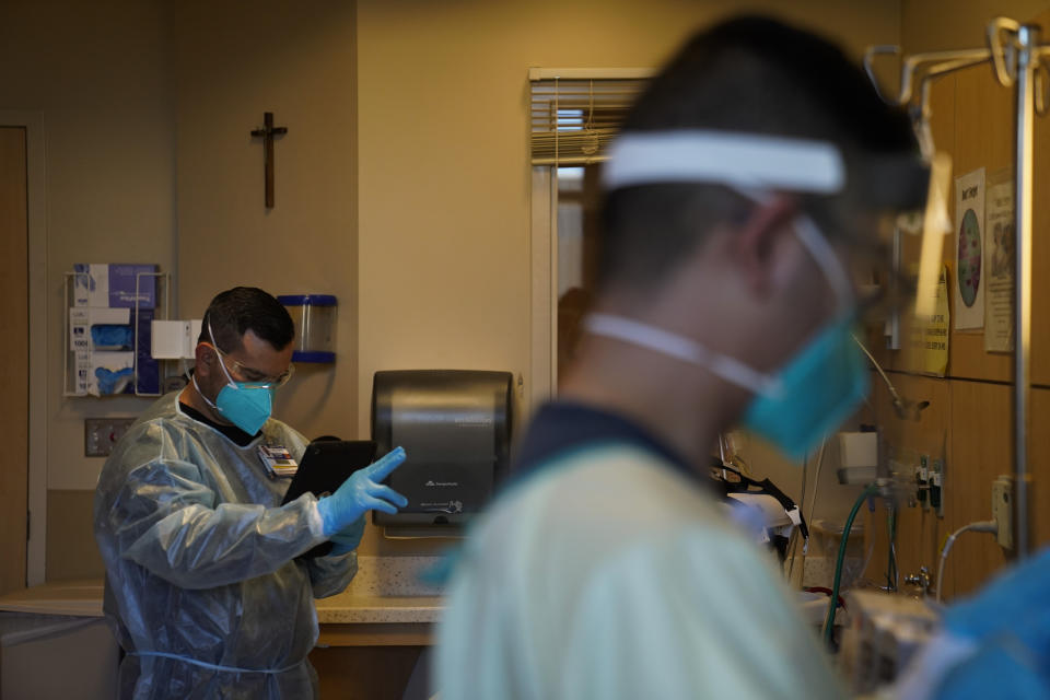 Chaplain Elias Mena, left, prays for a COVID-19 patient placed on comfort care as registered nurse Nikki De La Cruz, foreground, monitors the patient at Providence Holy Cross Medical Center in the Mission Hills section of Los Angeles on Friday, Jan. 15, 2021. As families are barred from visiting loved ones to curb the disease's spread, chaplains often are there to act as surrogates, holding the hands of the dying, praying with them and carrying iPads into hospital rooms to provide a real-time connection with grieving families. (AP Photo/Jae C. Hong)