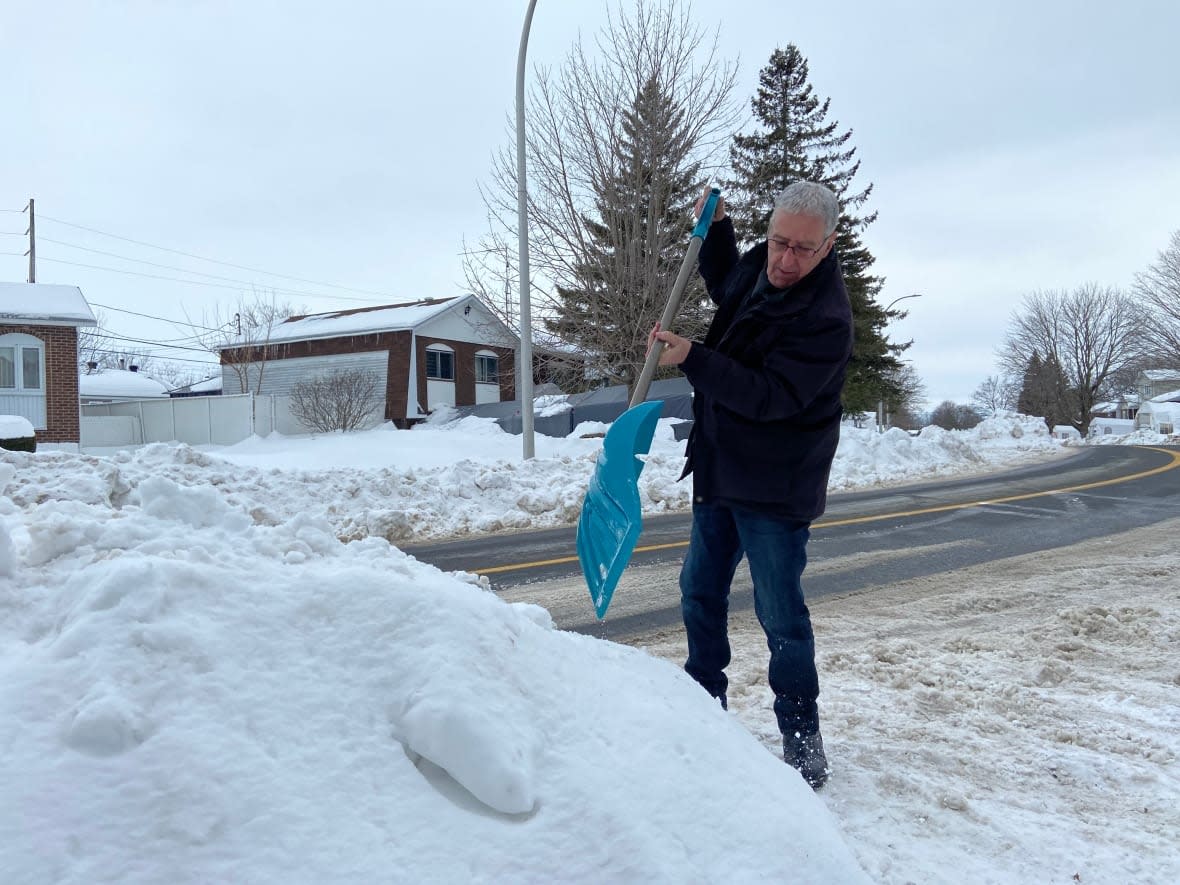 Daniel Poirier shovels snow on Albert-Einstein Boulevard in Châteauguay, Que., where he said the piles have been removed only once so far this winter. (Rowan Kennedy/CBC - image credit)