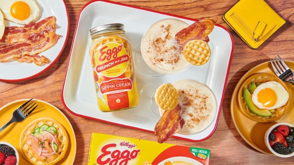 Eggo Brunch in a Jar Sippin Cream laying on its side on a plate with cocktails surrounded by plates of brunch food
