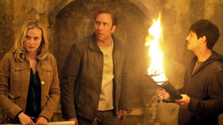 Three people stand together in a cave with fire.