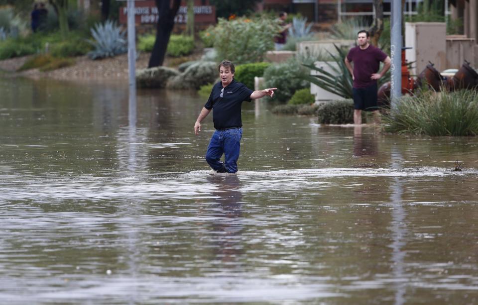 Pedestrians walk through a flooded street as they try to unclog storm drains during a flash flood as a result of heavy rains from tropical storm Rosa Tuesday, Oct. 2, 2018, in Phoenix. (AP Photo/Ross D. Franklin)