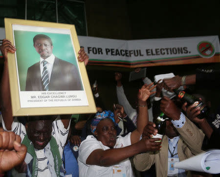 Patriotic Front General Secretary Davies Chama (L) celebrates while holding a portrait of President Edgar Chagwa Lungu after Lungu narrowly won re-election on Monday, in a vote his main rival Hakainde Hichilema rejected on claims of alleged rigging by the electoral commission, in the capital, Lusaka, Zambia, August 15, 2016. REUTERS/Jean Serge Mandela