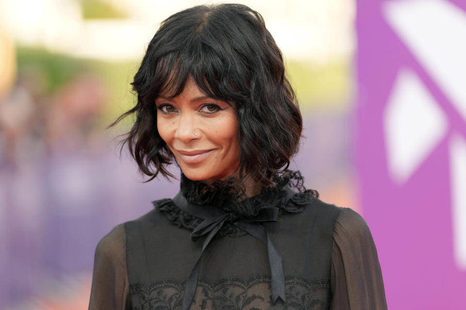 A woman with short, wavy black hair wearing a high-neck, lace-trimmed black dress at an event