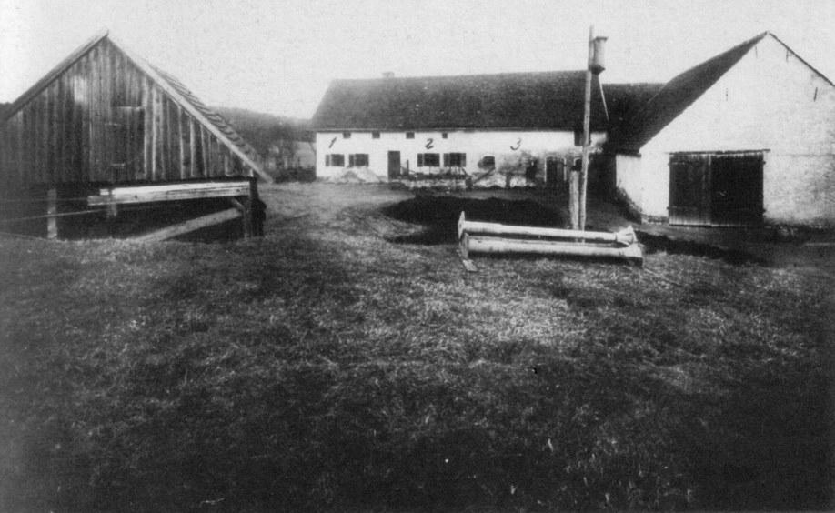 A historic black-and-white photo of several farm structures, including barns and a water well, on a grassy area. No people are present