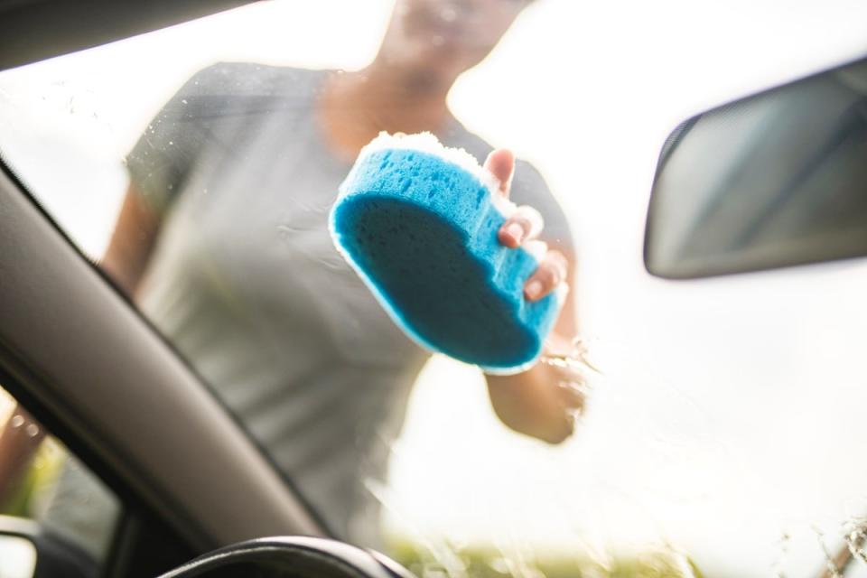 Woman rubbing car windshield with a blue and white sponge.