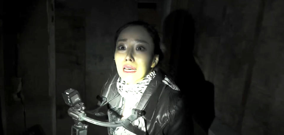 Person holding a camera in a dark, eerie setting with a frightened expression