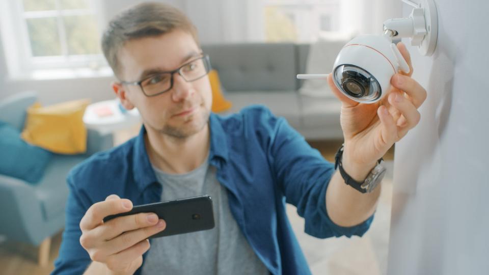 Young man holding a smartphone and checking his smart security camera.