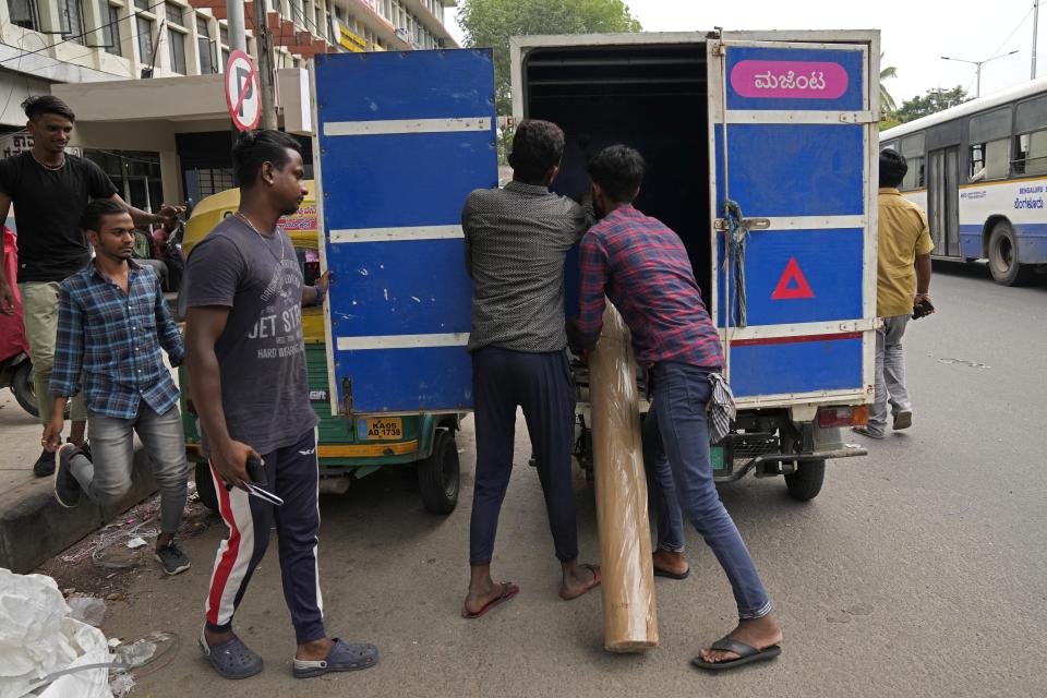 Balaji Premkumar, center, a 25-year-old rickshaw delivery driver who switched to an electric vehicle this year, watches as staff of a furnishing outlet unload goods delivered by him in Bengaluru, India, Monday, May 29, 2023. At most traffic stops he's surrounded by gas-powered three-wheelers that rumble and rattle, spewing thick smoke into the air — something that his used to do, too, before he went electric. (AP Photo/Aijaz Rahi)