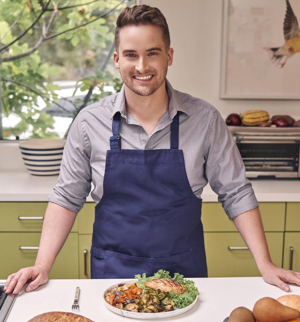 "Tasting History" star Max Miller in a blue apron behind a counter with a plate of food on it