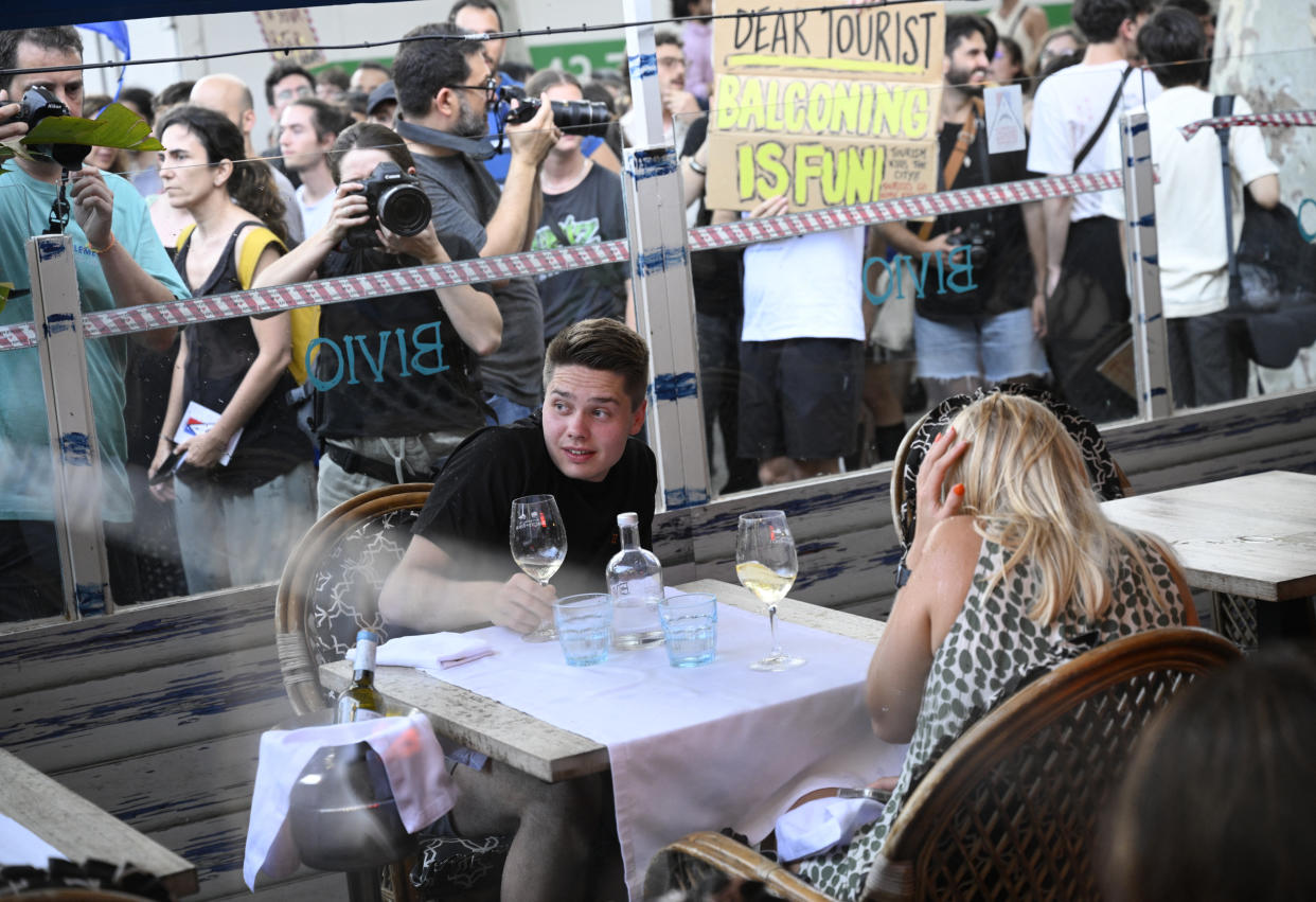 TOPSHOT - Demonstrators put symbolic cordon on a bar-restaurant window during a protest against mass tourism on Barcelona's Las Ramblas alley, on July 6, 2024. Protests against mass tourism have multiplied in recent months across Spain, the world's second-most visited country. (Photo by Josep LAGO / AFP) (Photo by JOSEP LAGO/AFP via Getty Images)