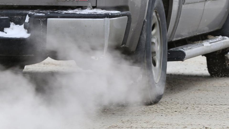 Car exhaust is pictured on a snowy day. Idling automobile. 