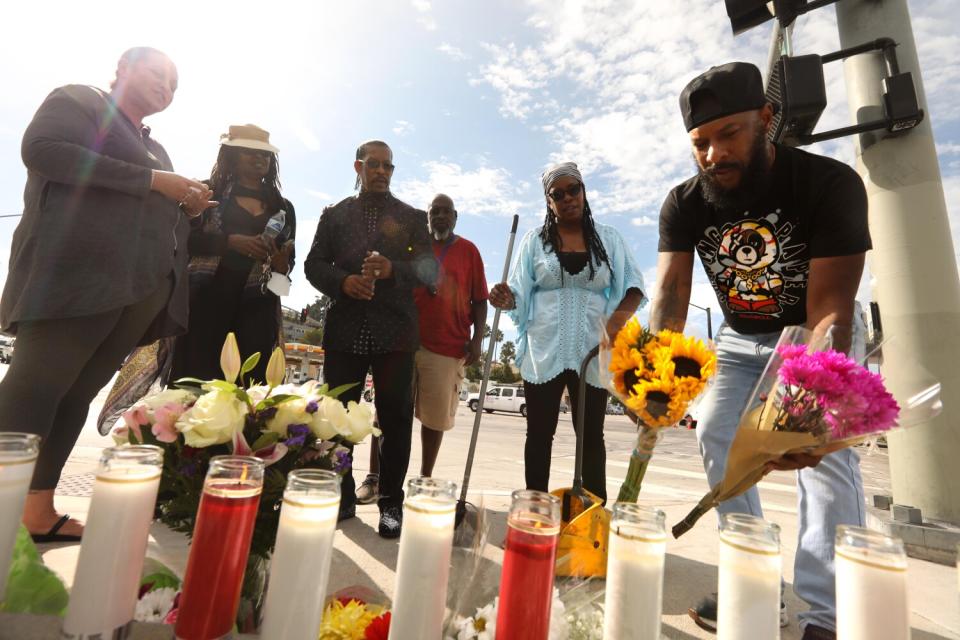 People gather and leave flowers and candles at a memorial.