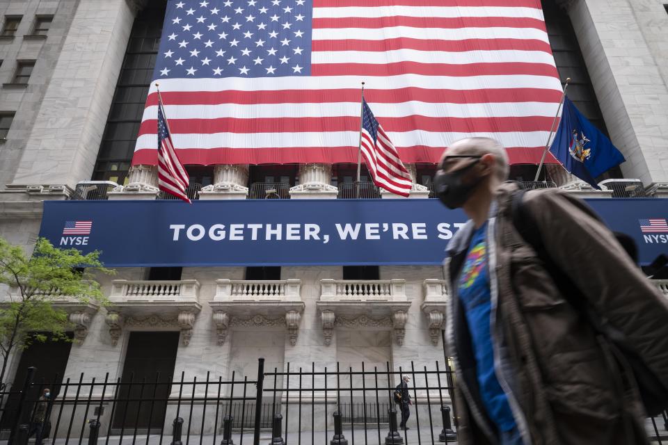 A man wearing a protective face mask passes the New York Stock Exchange, Tuesday, May 26, 2020, as employees arrive for the partial reopening of the trading floor. (AP Photo/Mark Lennihan)