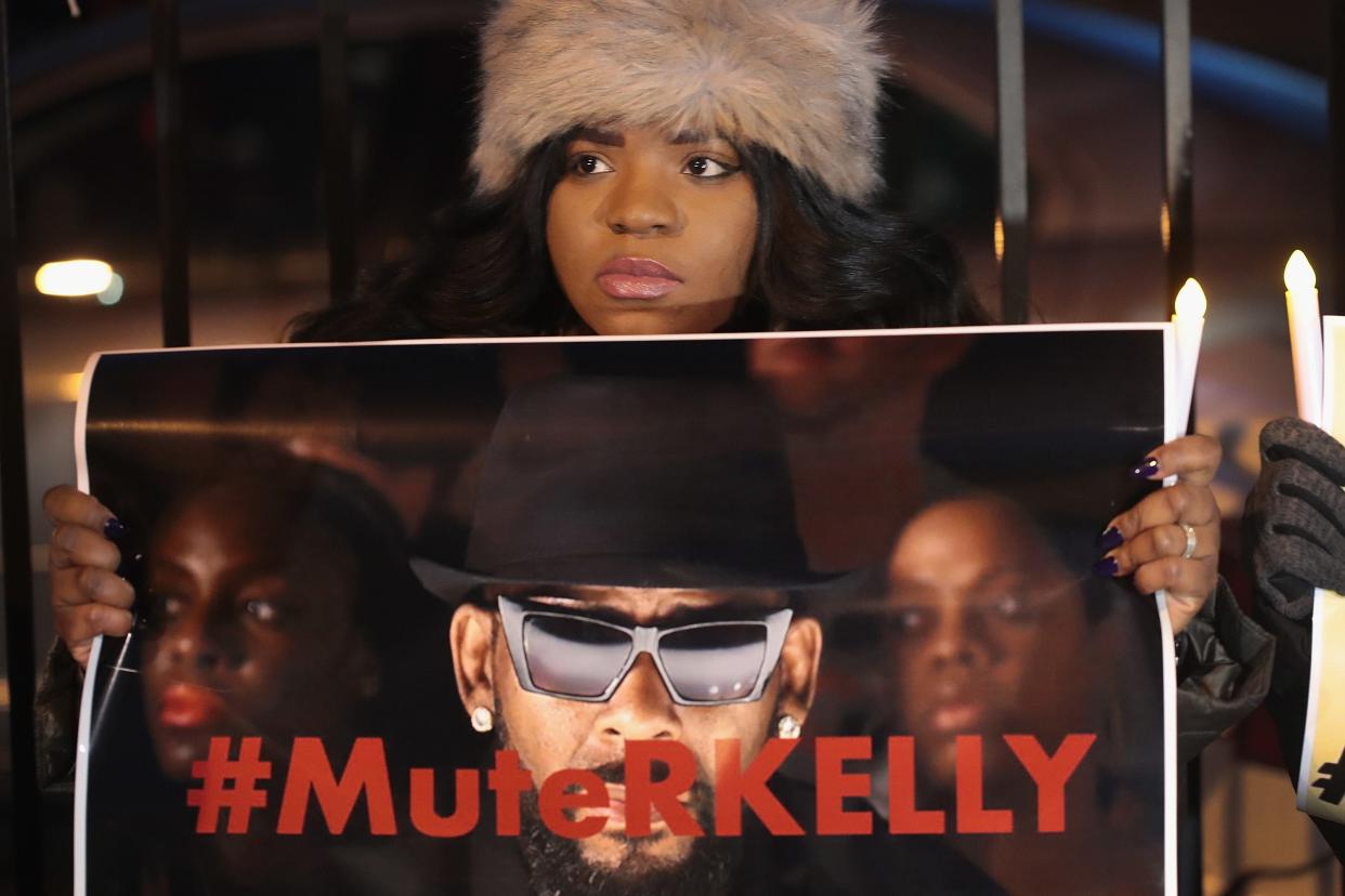 Black woman protesting, holding up sign that says hashtag mute R. Kelly.