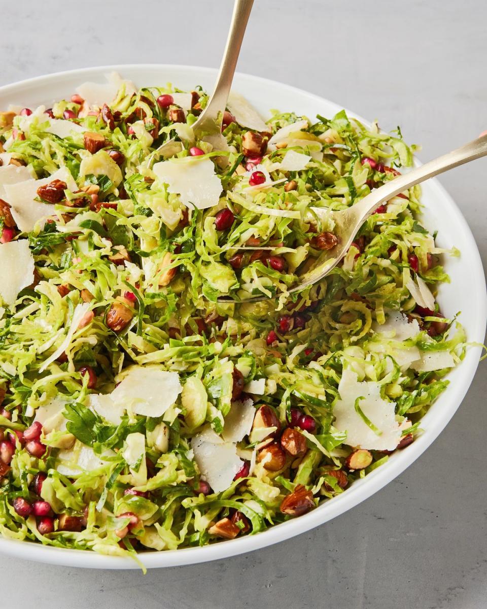 shaved brussels sprouts with pomegranates, shaved parmesan, and chopped toasted almonds in a white bowl