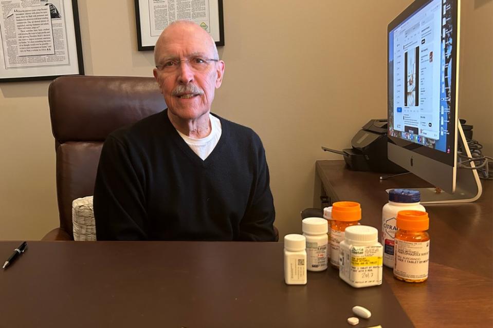 David Mitchell, founder of Patients for Affordable Drugs, sits in his home office. Beside him are some of the many drugs he takes to treat multiple myeloma and other conditions. (Arthur Allen/KFF Health News)