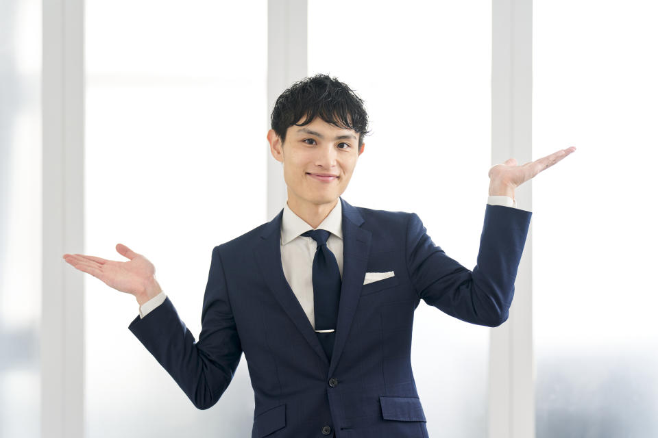 Man wearing a suit gesturing with both hands, standing in a bright office