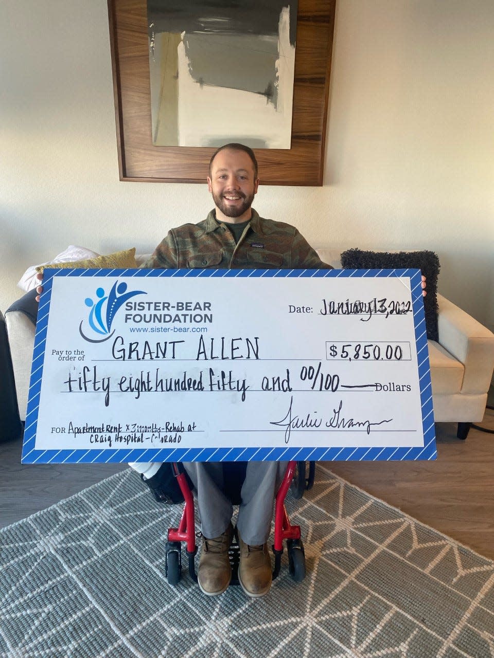 Grant Allen displays the check awarded to him by the Sister-Bear Foundation to cover the cost of his rent while he attends his rehabilitative therapy in Denver.