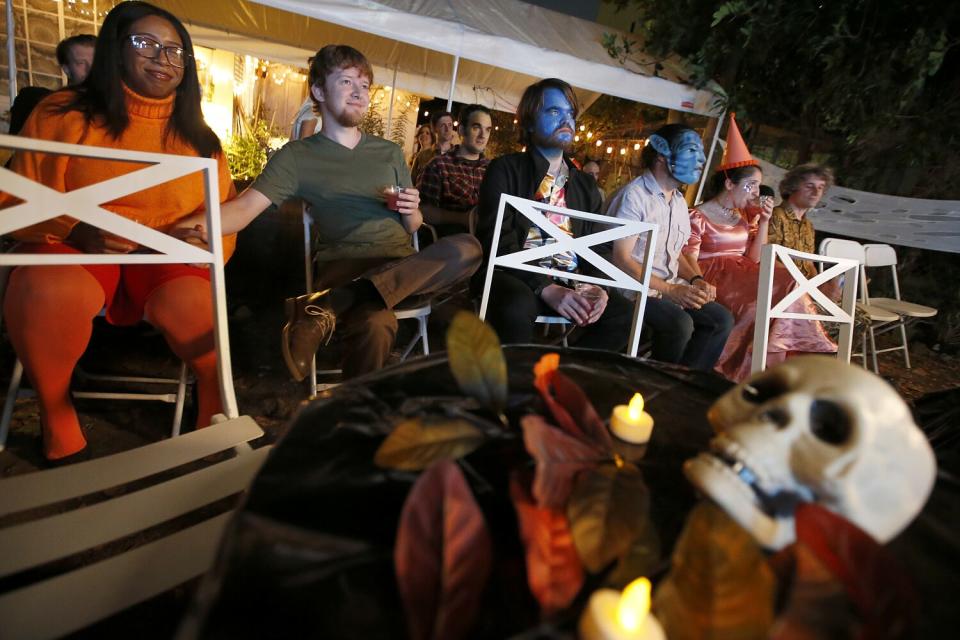 People dressed up sit in close-together chairs in a backyard