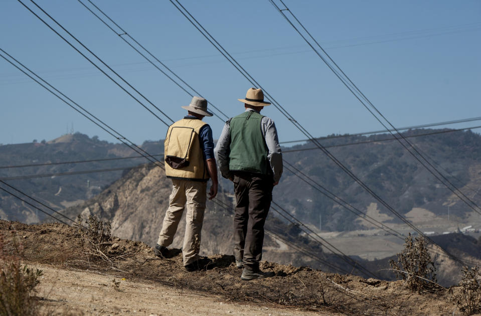 FILE - In this Oct. 15, 2019 file photo, fire investigators examine the scene around a transformer tower in Sylmar, Calif., suspected of being responsible for starting the Saddleridge fire. Southern California Edison will pay $2.2 billion to settle insurance claims from a deadly, destructive wildfire sparked by its equipment in 2018, the utility announced Monday, Jan. 25, 2021. (AP Photo/Christian Monterrosa, File)