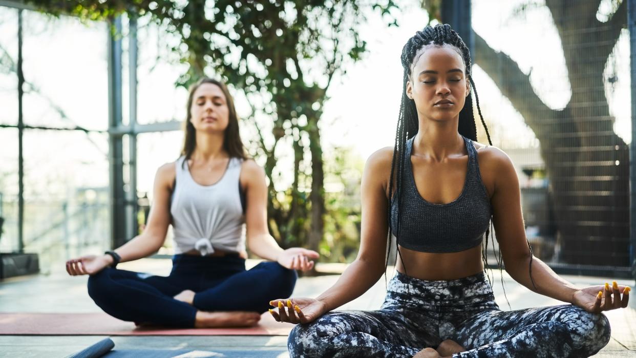 Young woman practicing lotus position with friend on porch.