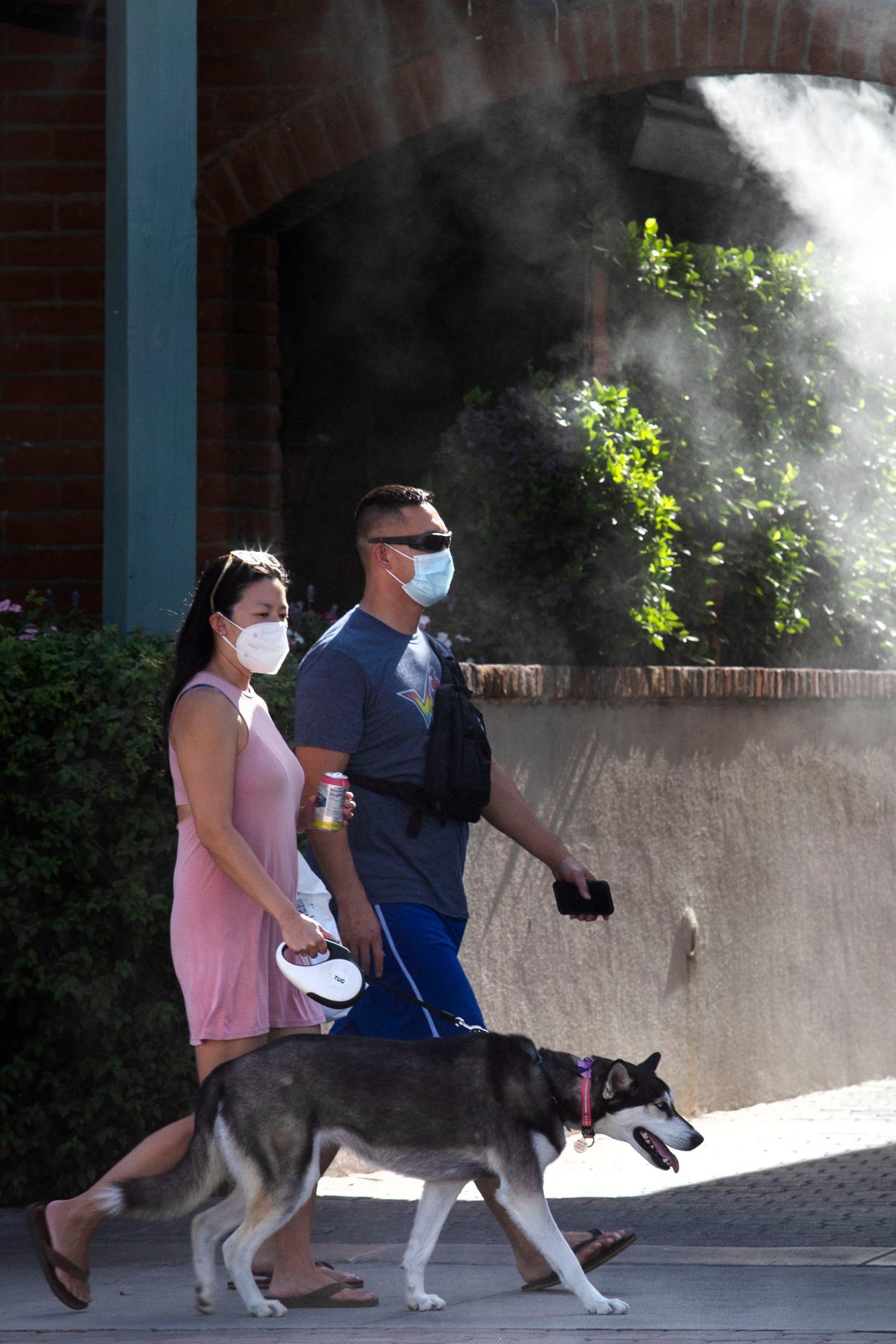 People walk their dog walk under misters on a triple-digit day along Palm Canyon Drive in downtown Palm Springs, Calif., on Saturday, June 5, 2021. The Coachella Valley will get a break from summer-like heat this week with temperatures expected to peak in the 90s through Thursday before triple digits return by the weekend.
